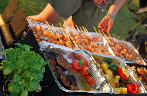 Przygotowywanie grillowanych szaszłyków z krewetek i warzyw (bakłażan, papryka, ziemniaki) serwowanych w aluminiowych tackach, dekorowanych świeżą bazylią.