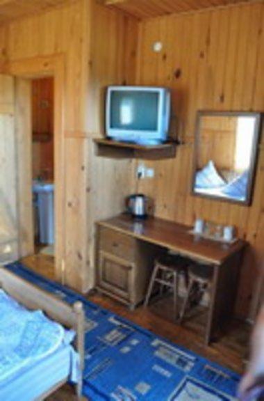 Wnętrze pokoju w drewnianym stylu z telewizorem, biurkiem, czajnikiem elektrycznym i łazienką w tle, sugerujące zakwaterowanie podczas wyjazdu 'Ukraina SKI Tour'.