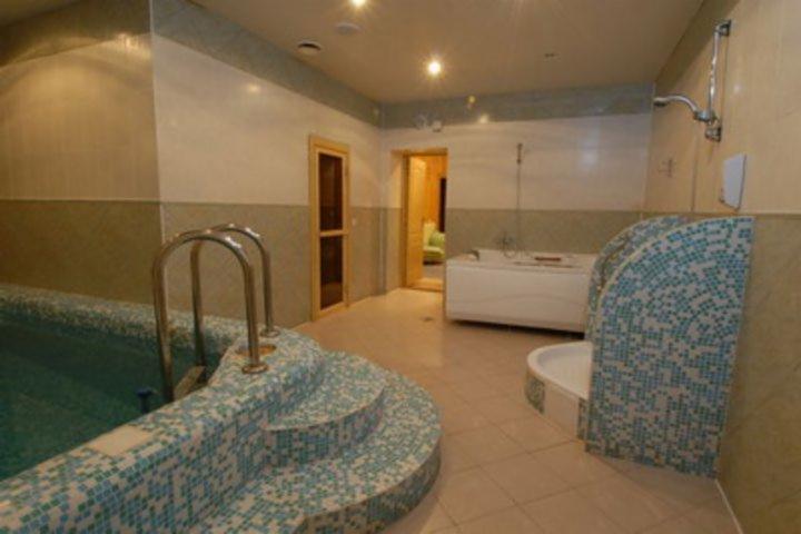 Wnętrze luksusowego spa z basenem wyłożonym mozaiką w odcieniach błękitu, obok wanna z hydromasażem i wejście do sauny.