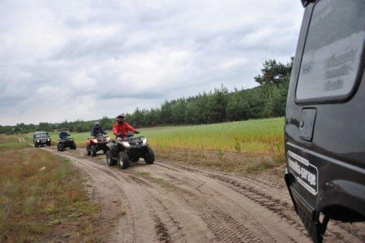 Off-roadowa wyprawa: grupa osób na quadach i samochodzie terenowym jedzie po piaszczystej drodze w kierunku lasu, widok zza samochodu.
