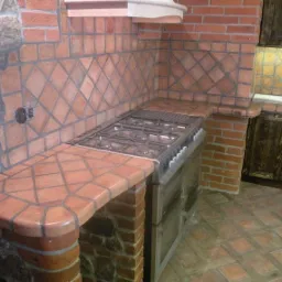 Rustykalna kuchnia z ceglaną zabudową, terakotową mozaiką na ścianie i blacie, oraz stalową kuchenką gazową.