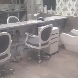 Wnętrze salonu fryzjerskiego z trzema białymi fotelami z szarymi siedziskami, białą myjnią fryzjerską i szarą ladą z lustrem, w tle tapeta w delikatny wzór.