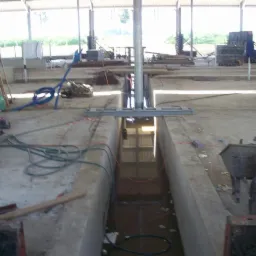 Wnętrze budowanej obory z wykopanym kanałem na fundamenty, widoczne szalunki, rury i taczka, w tle konstrukcja dachu.