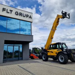Żółty wózek widłowy Dieci na tle nowoczesnego budynku z logo FLT Grupa i odbijającym się niebem w oknach. W tle widoczny pomarańczowy wózek.