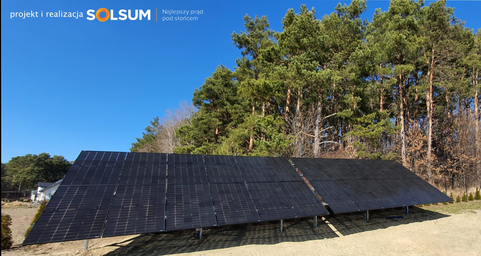 Instalacja paneli słonecznych z logo firmy SOLSUM na tle lasu i błękitnego nieba.