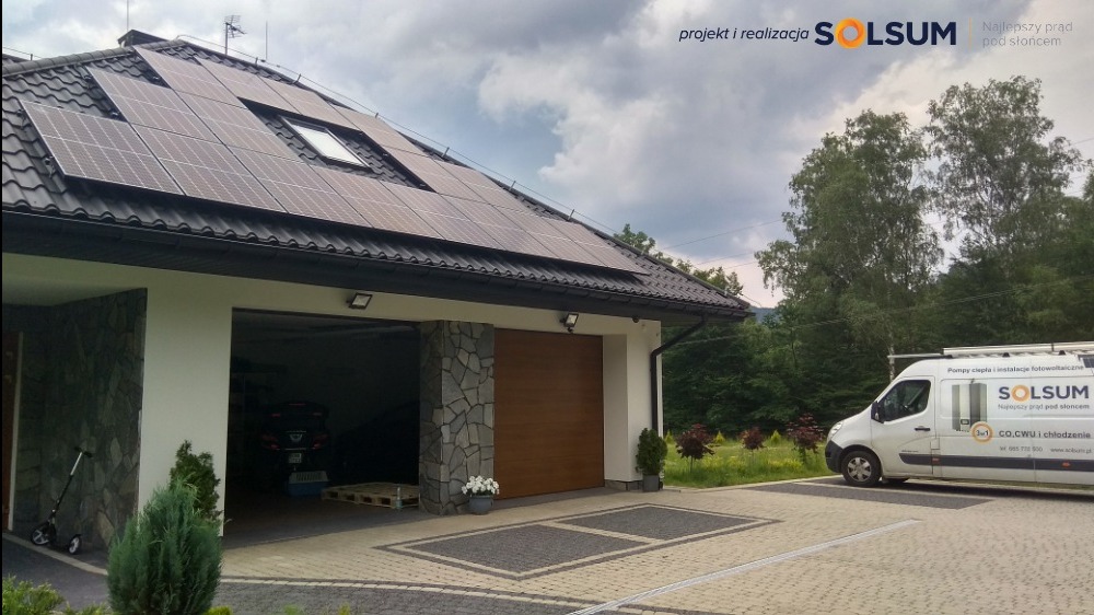 Panele słoneczne na dachu domu z dwustanowiskowym garażem, biała furgonetka z logo firmy na podjeździe.