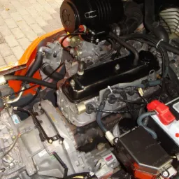 Szczegółowe ujęcie silnika wózka widłowego Toyota 7 FGF 15 z widoczną skrzynią biegów, akumulatorem i przewodami, umieszczonego na zewnątrz na brukowanej powierzchni.