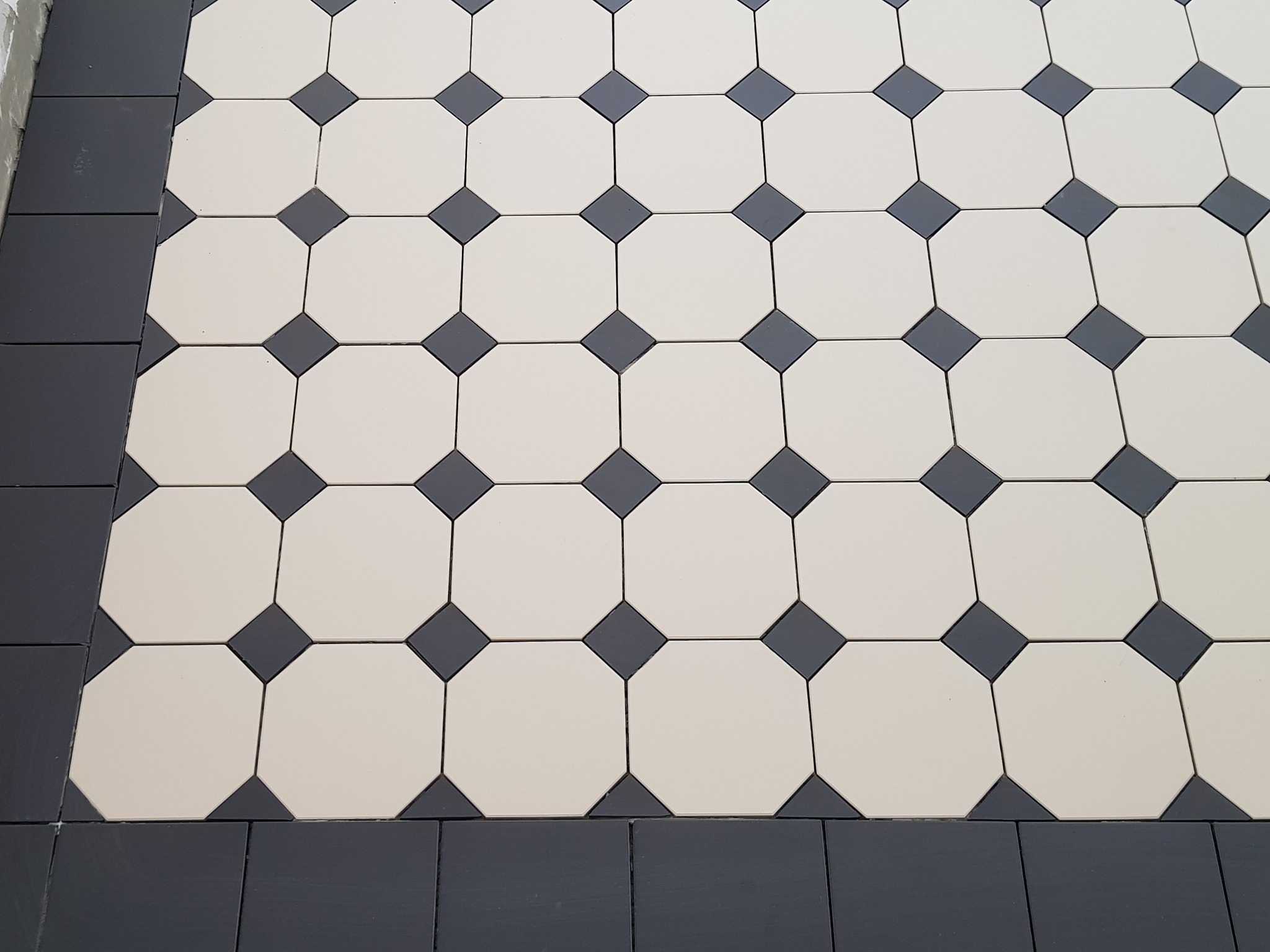 Ułożona podłoga z jasnych, oktagonalnych płytek z ciemnymi, kwadratowymi wstawkami i obramowaniem z ciemnych płytek.