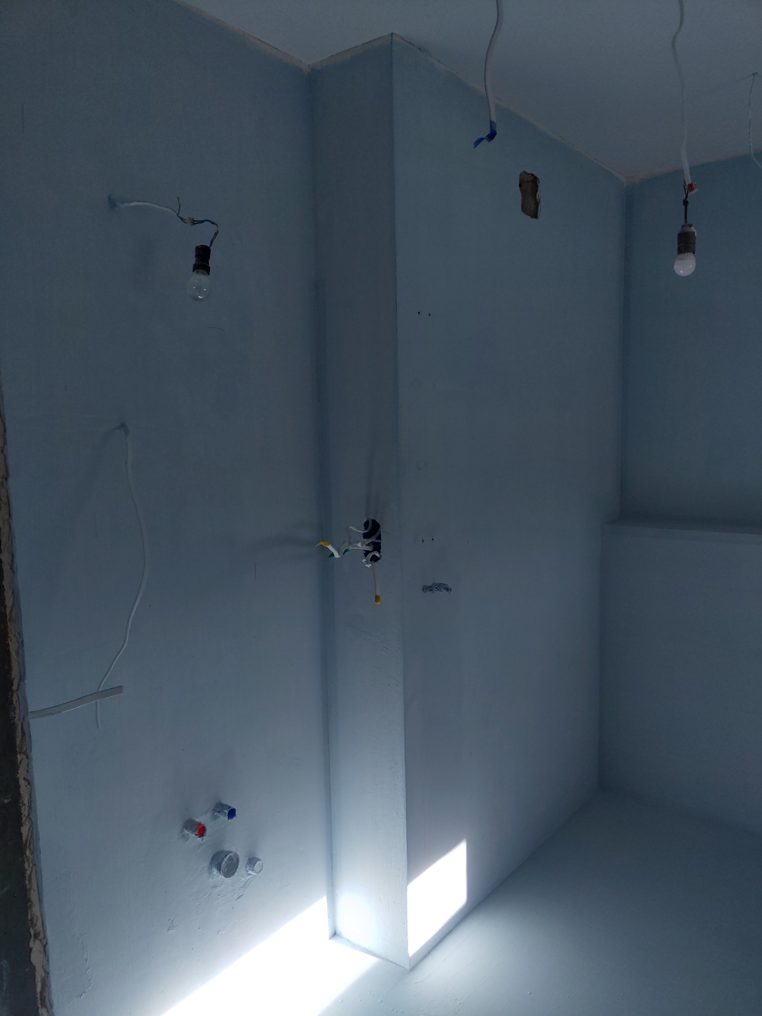 Niebieskie wnętrze po malowaniu, widoczne wystające kable, rury i niedokończone instalacje elektryczne i hydrauliczne. Świeże malowanie ścian i podłogi.