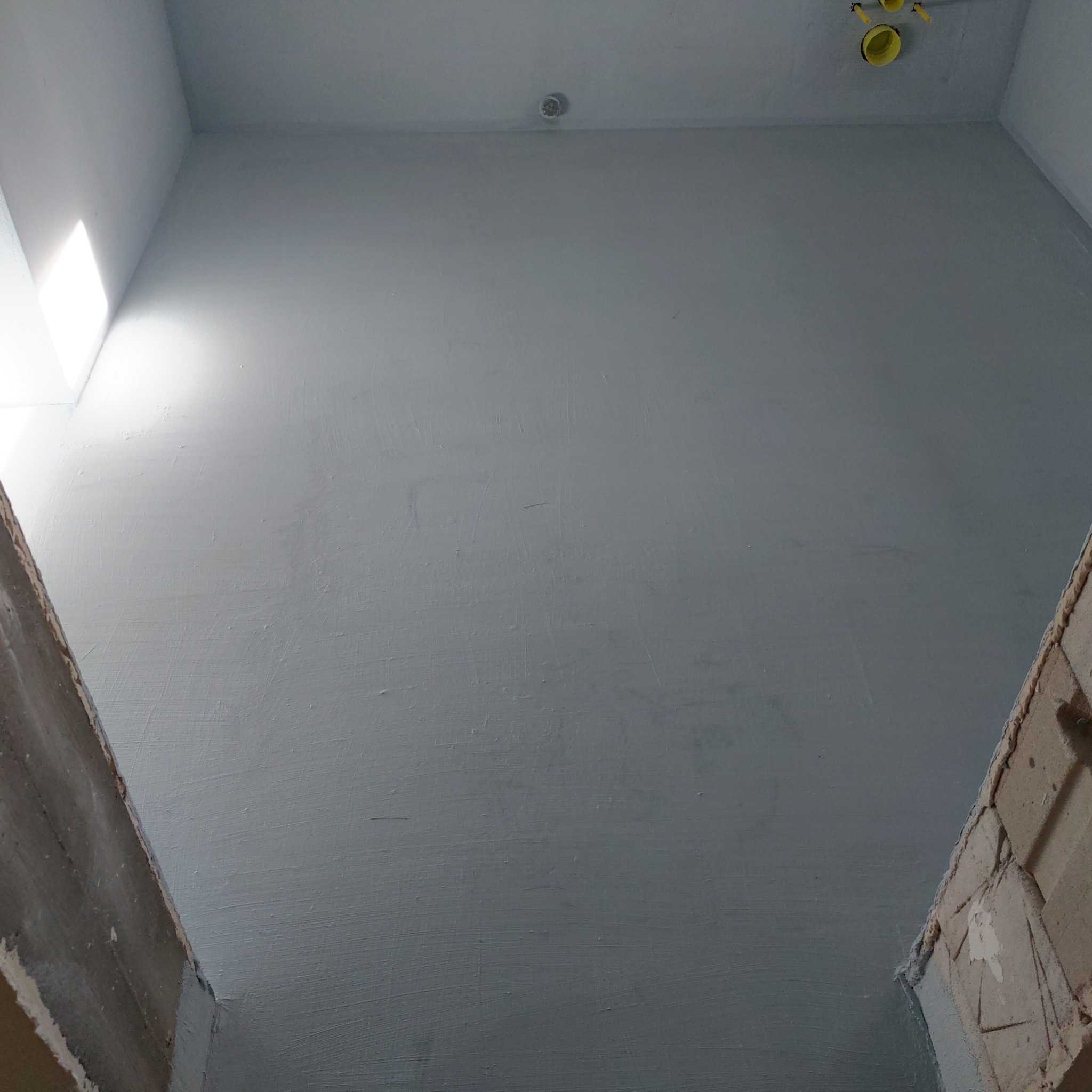 Wnętrze w trakcie malowania: szare ściany, widoczne fragmenty surowych ścian i instalacje elektryczne. Ujęcie od dołu, światło wpada z góry.