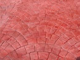 Czerwona, odciśnięta w betonie nawierzchnia w kształcie wachlarzy, imitująca kostkę brukową. Widoczne nieregularności i różnice w odcieniach koloru.