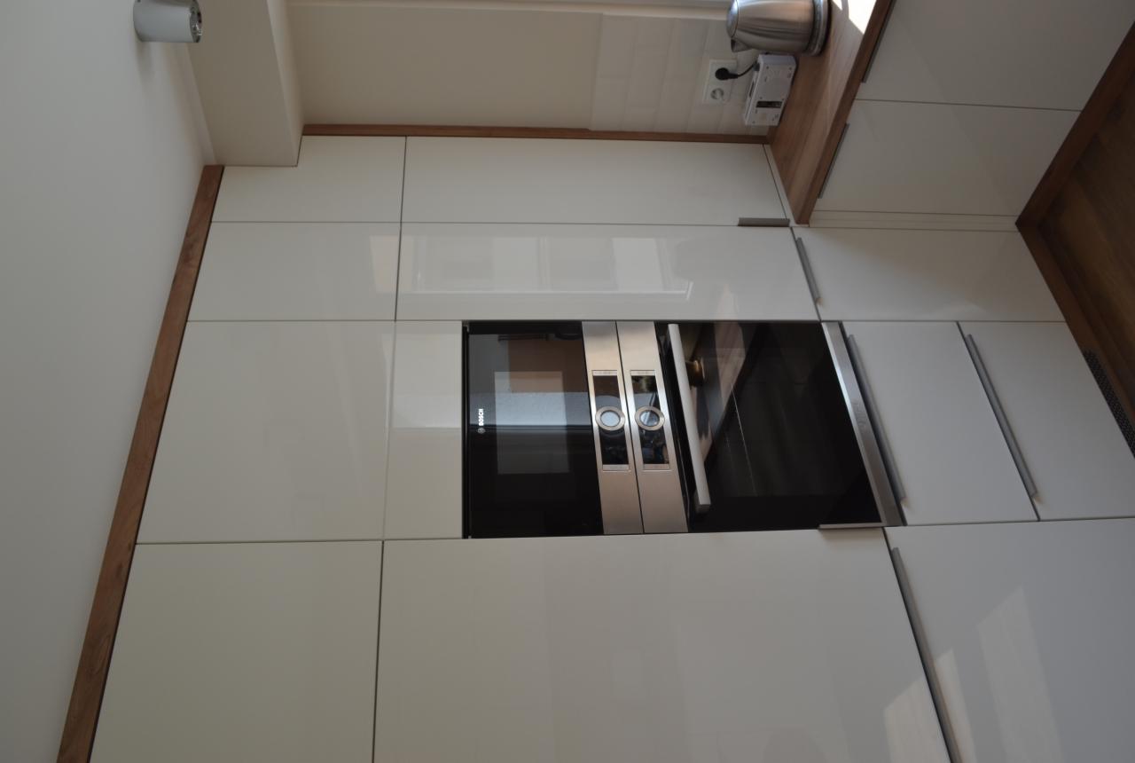 Nowoczesna kuchnia z białymi, lakierowanymi frontami szafek, wbudowanym piekarnikiem marki Bosch i drewnianym blatem.