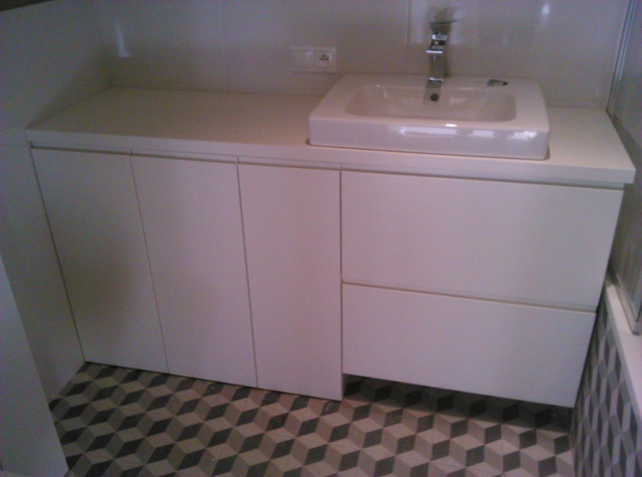 Biała umywalka nablatowa z chromowaną baterią na szafce z frontami bez uchwytów, wzorzysta podłoga w łazience.