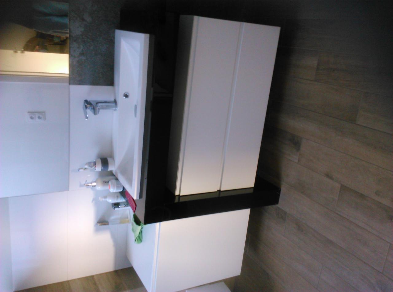 Nowoczesna łazienka z białą umywalką nablatową, szafką z czarnym blatem i białymi frontami, oraz drewnopodobną podłogą.