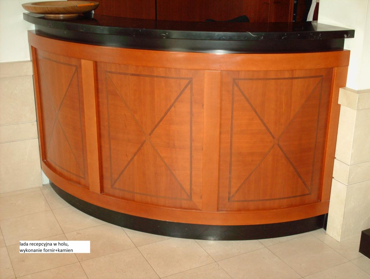 Zaokrąglona lada recepcyjna z forniru z geometrycznym wzorem i czarnym blatem z kamienia, ustawiona na jasnej podłodze z płytek.