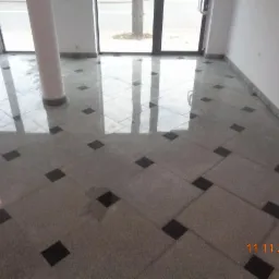 Wyłożona szaro-czarnymi płytkami podłoga w jasnym, pustym pomieszczeniu z dużymi oknami i kolumną po lewej stronie.