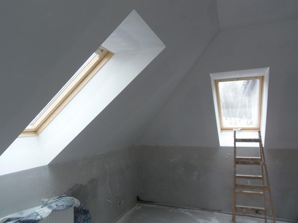 Poddasze w trakcie adaptacji w Warszawie, widoczne dwa okna dachowe, ściany przygotowane do malowania, drabina oparta o ścianę, widoczne niedoskonałości ścian przed wykończeniem.