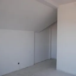 Białe, świeżo pomalowane wnętrze poddasza z widocznymi gniazdkami elektrycznymi i surową podłogą. Ściany gładkie, gotowe do dalszych prac wykończeniowych.