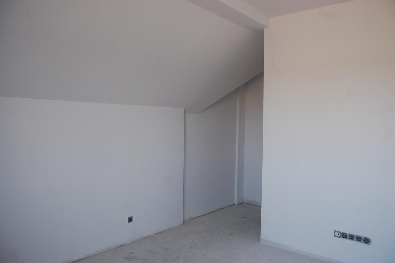 Białe, świeżo pomalowane wnętrze poddasza z widocznymi gniazdkami elektrycznymi i surową podłogą. Ściany gładkie, gotowe do dalszych prac wykończeniowych.