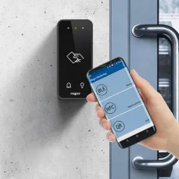 Czarny czytnik kart dostępu Roger zamontowany na szarej ścianie, obok niego dłoń trzyma smartfon z aplikacją Roger Mobile Key wyświetlającą opcje połączenia BLE, NFC i QR, widoczny fragment...