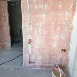 Crado - Wewnętrzne ściany z czerwonej cegły z widoczną instalacją elektryczną w trakcie montażu, z puszkami elektrycznymi i przewodami, oraz częściowo wykończona ściana gipsowa i pęknięcie w wylewce...