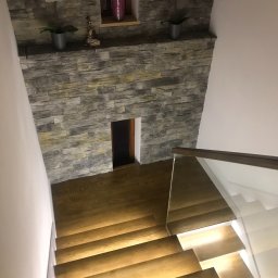 Crado - Schody drewniane z podświetleniem LED, kamienna ściana z półką dekoracyjną i kwiatami w doniczkach, widok z góry.