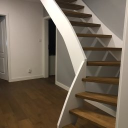 Crado - Drewniane schody z białymi balustradami w nowoczesnym wnętrzu, widok z dołu, parkiet na podłodze, drzwi w tle.