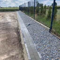 P.H.U Waldemar Ginter - Świeżo ułożony chodnik z szarych kostek brukowych obok metalowej siatki ogrodzeniowej i wysypanego żwiru, z widoczną rurą kanalizacyjną i przygotowanym terenem pod dalsze prace.