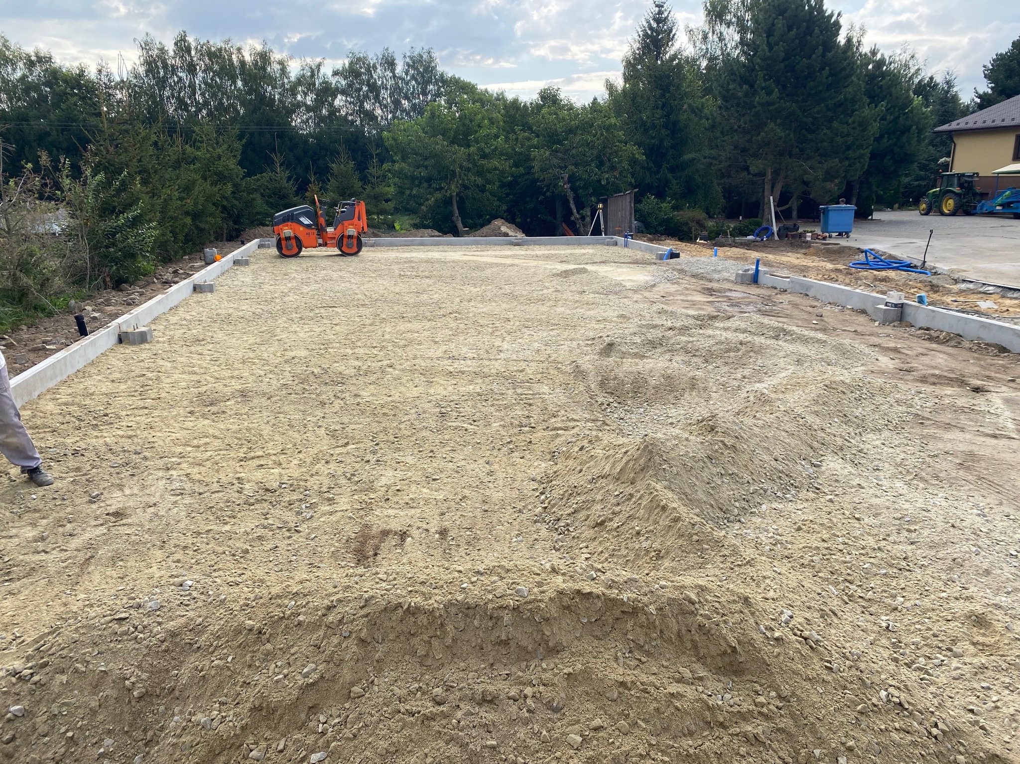Przygotowany teren pod budowę z fundamentami, ubijarką i widoczną pryzmą piasku.