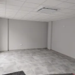 Wnętrze biura po remoncie z szarymi ścianami, płytkami podłogowymi imitującymi kamień i podwieszanym sufitem z kratownicą oraz klimatyzacją kasetonową.