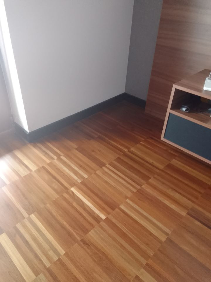 Parkiet z jasnego drewna ułożony w kwadraty, widok z góry w rogu pokoju, ciemna listwa przypodłogowa.