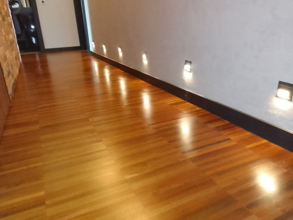 Parkiet ułożony w jodełkę o ciepłym odcieniu drewna, oświetlony punktowymi lampami ściennymi, widok na korytarz.