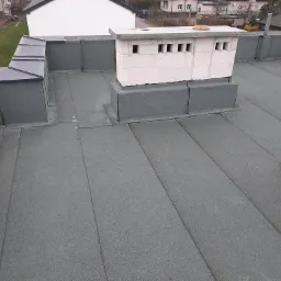 Płaski dach pokryty papą termozgrzewalną z kominem wentylacyjnym z betonu komórkowego w trakcie budowy.