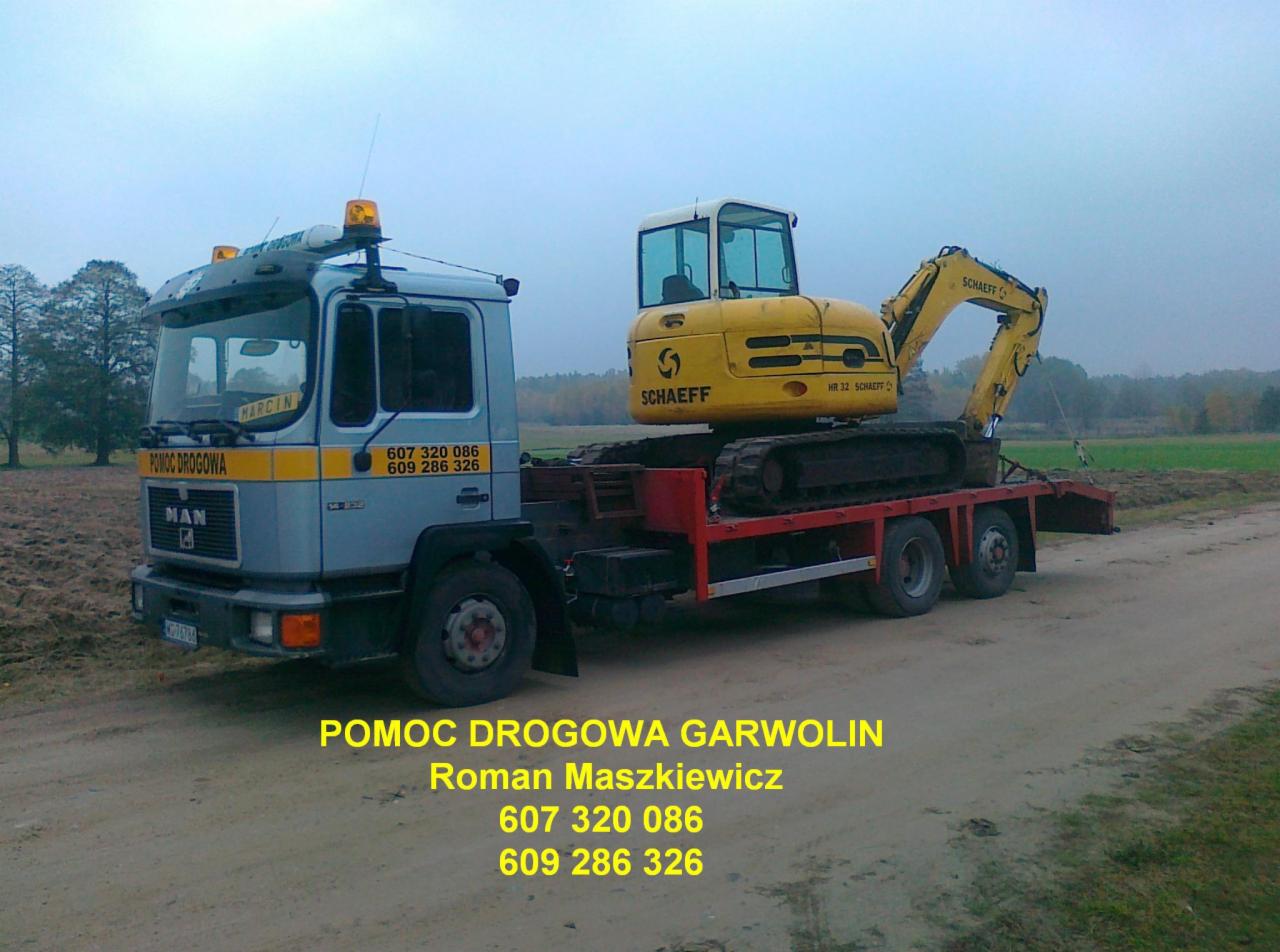 Laweta MAN z żółtą koparką Schaeff HR 32 na czerwonej platformie, widoczne numery kontaktowe i nazwa 'Pomoc Drogowa Garwolin'.