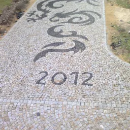Granitowa ścieżka z mozaiką smoka i rokiem 2012, wykonana z drobnej kostki. Nieregularny kształt ścieżki, szara kostka, czarny wzór smoka. Unikalny projekt.