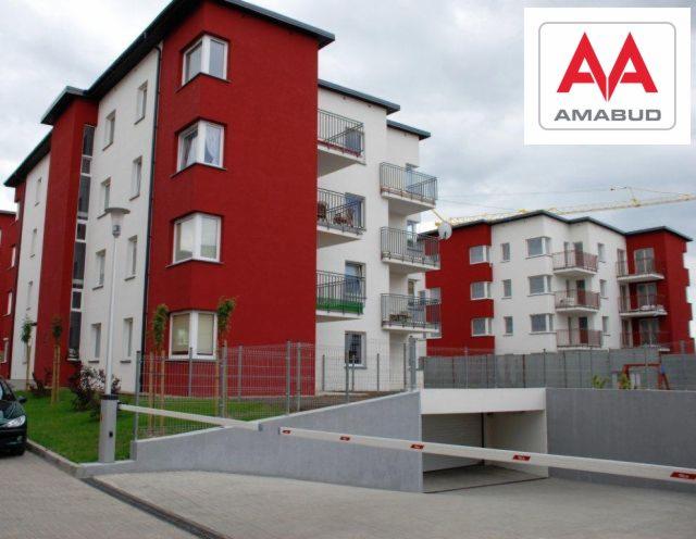 Nowoczesne, wielorodzinne budynki mieszkalne z balkonami, pomalowane na biało i czerwono, z podziemnym parkingiem i szlabanem wjazdowym, logo dewelopera w prawym górnym rogu.