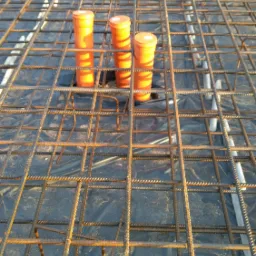 Zbrojenie pod wylewkę betonową z widocznymi pomarańczowymi rurami instalacji ogrzewania podłogowego na folii izolacyjnej.