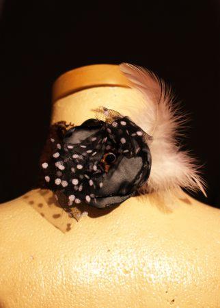 Czarna opaska z białymi kropkami, piórkiem i siateczką, umieszczona na manekinie.