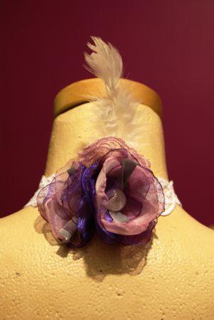 Dekoracyjny choker z fioletowo-różowymi kwiatami z organzy i piórkiem, umieszczony na manekinie.