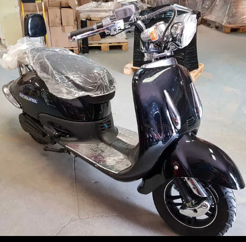 Czarny skuter elektryczny marki Securil z chromowanymi elementami, zapakowany w folię ochronną, w magazynie z kartonami w tle.