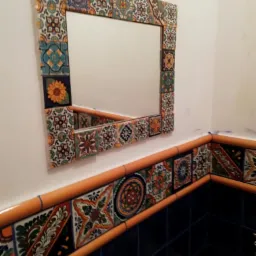 Umywalka w łazience z ciemnymi płytkami i lustrem w ramie z dekoracyjnych płytek ceramicznych w stylu meksykańskim.