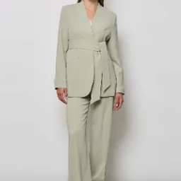 Modelka w pistacjowym damskim garniturze z wiązanym paskiem, prezentacja na białym tle.
