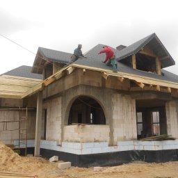 JARSTOL - Budowa domu: Murarze pracują na dachu pokrytym papą, widoczne ściany z betonu komórkowego, fundamenty ocieplone styropianem, rusztowania i hałda piasku.