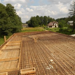 JARSTOL - Zbrojenie stropu na deskowaniu, widok z góry na siatkę z prętów stalowych i drewniane szalunki, w tle zabudowa jednorodzinna i zieleń