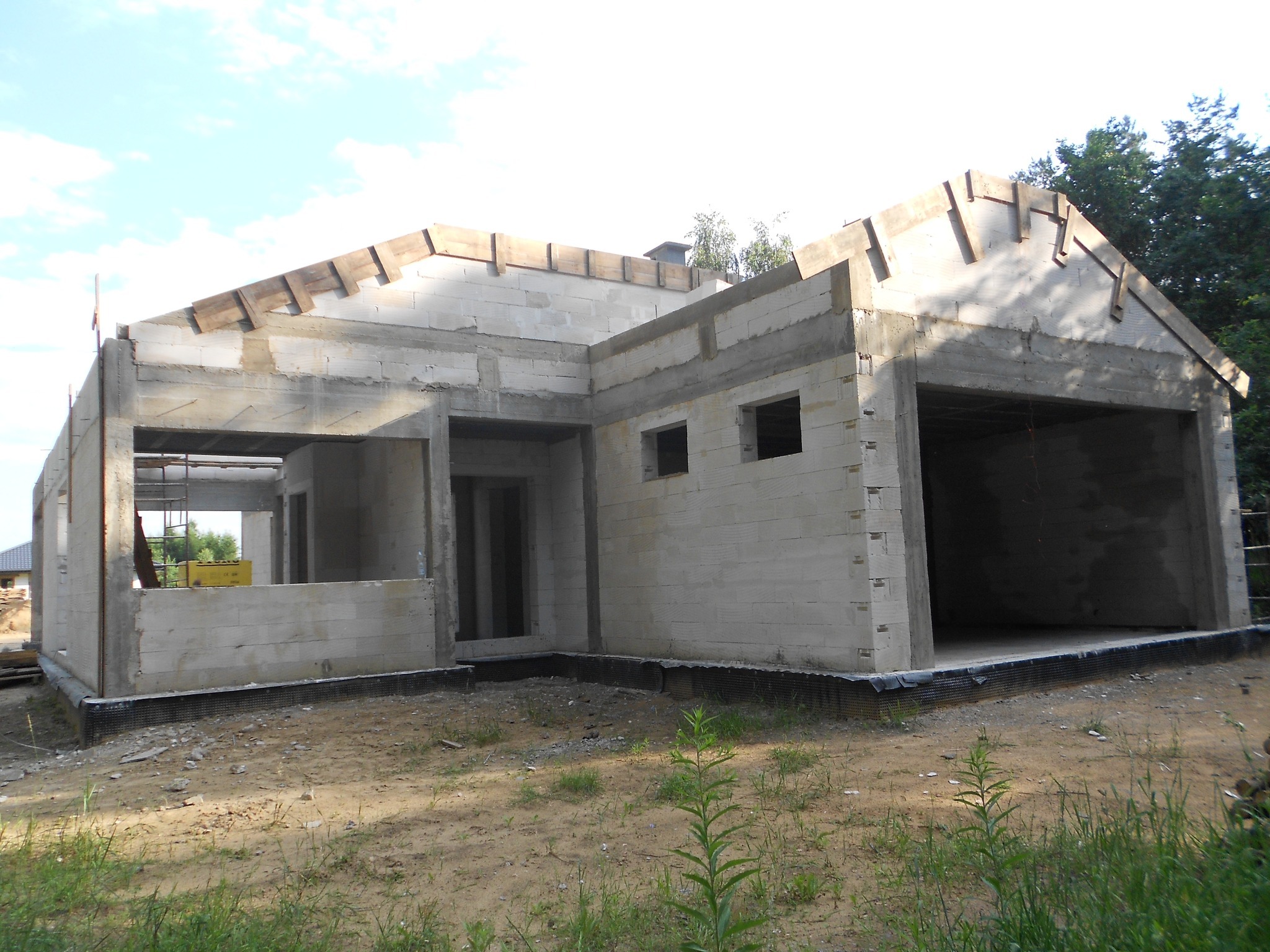 Surowy stan domu jednorodzinnego z betonu komórkowego z widocznymi elementami konstrukcyjnymi dachu i hydroizolacją fundamentów.