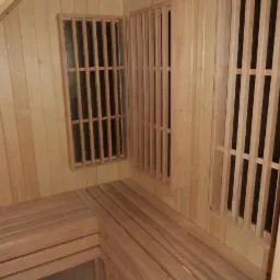 Wnętrze sauny z drewnianymi ławkami i ażurowymi panelami ściennymi, oświetlone górnym światłem.