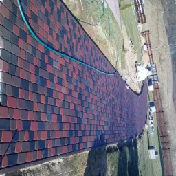 Ułożona, kolorowa kostka brukowa tworząca ścieżkę w ogrodzie, widok z góry. Częściowo widoczne materiały budowlane i trawnik. Nietypowy wzór ułożenia kostki.