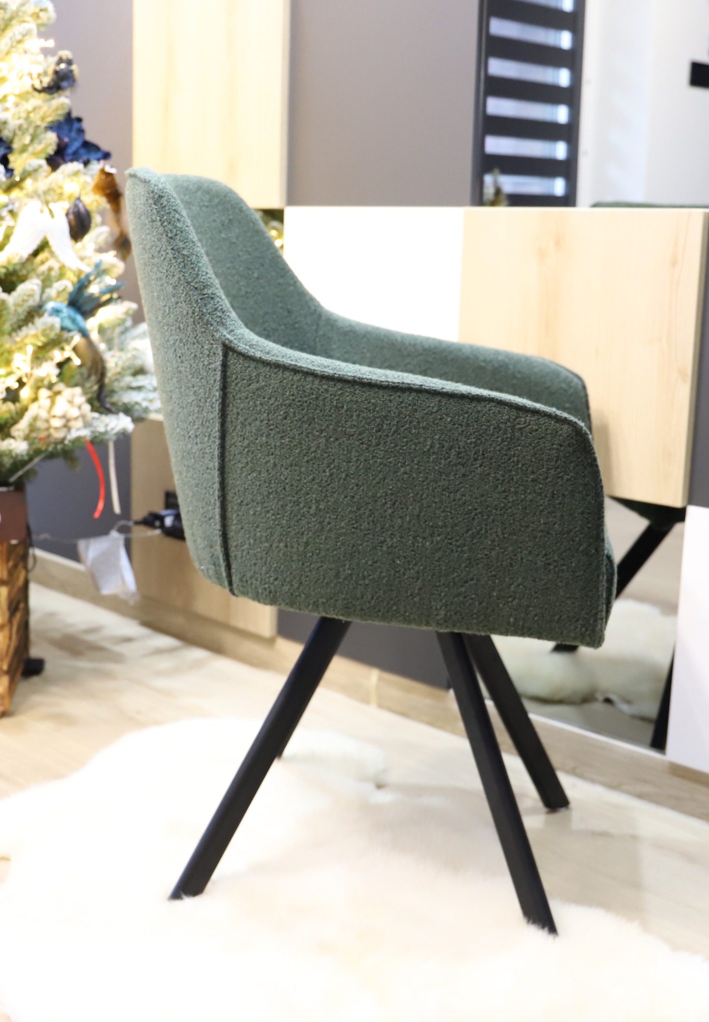Zielone krzesło tapicerowane z czarnymi nogami na tle choinki i jasnych mebli.