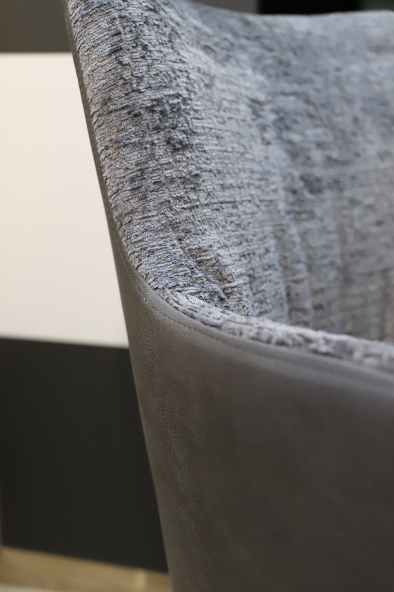 Detale wykończenia krzesła: szara tapicerka o wyraźnej fakturze połączona z gładką, ciemnoszarą skórą ekologiczną, widoczne precyzyjne szwy