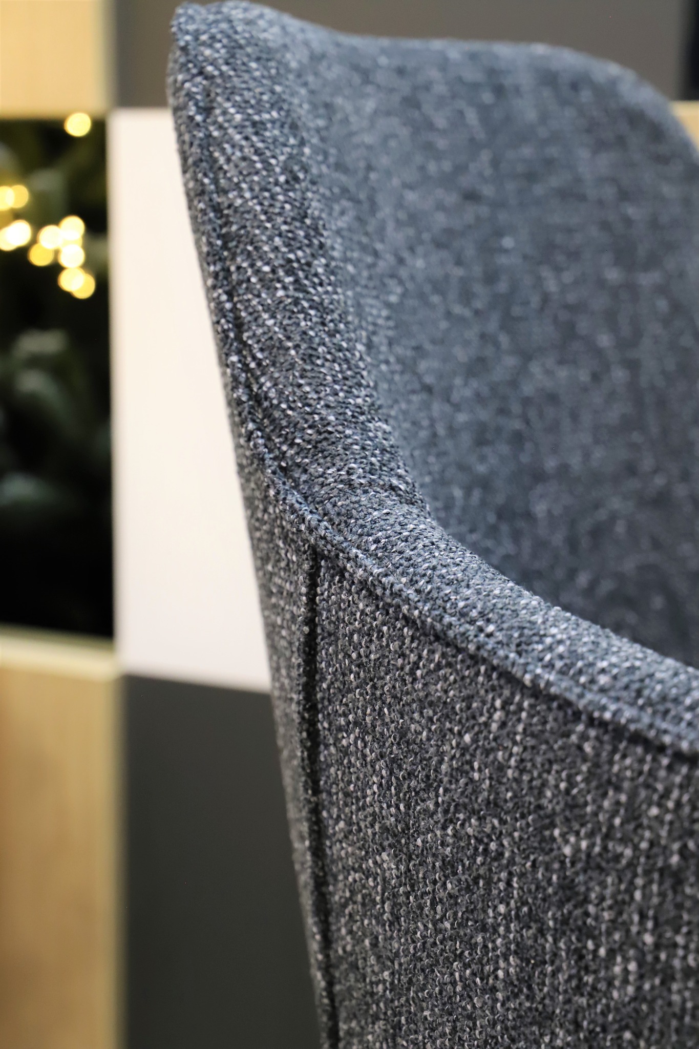Detale wykończenia tapicerowanego krzesła w odcieniach szarości, widoczny szew i faktura materiału, w tle dekoracje świetlne.